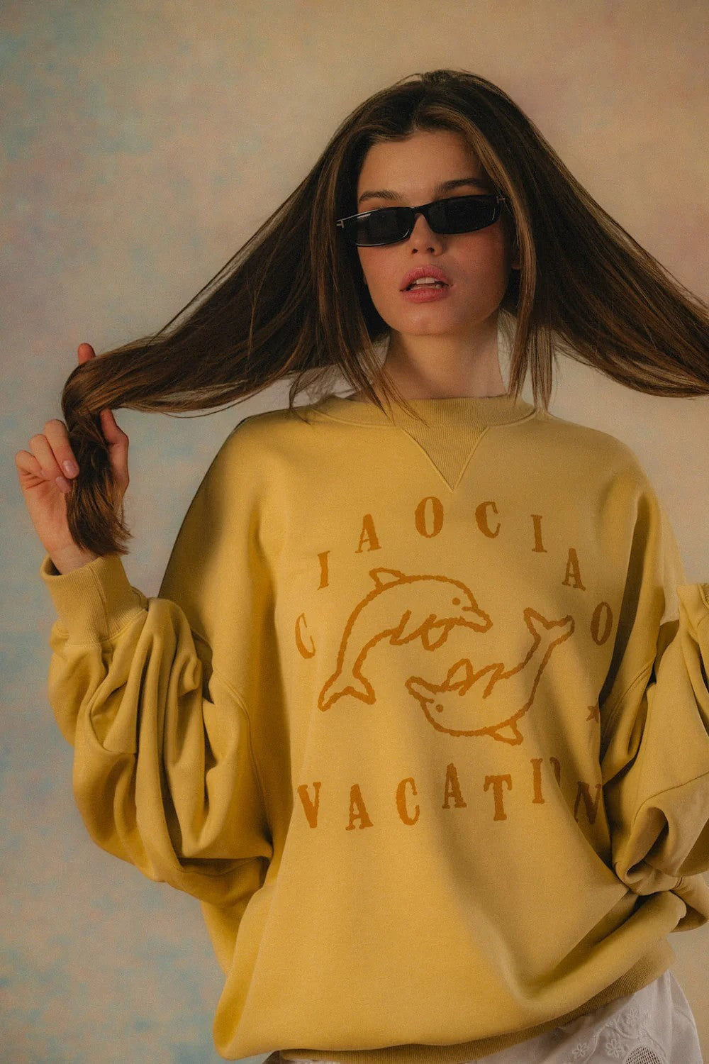 Keel Surf & Supply yellow cotton Delfino sweater with dolphin graphic and 'CIAO VACATION' text. Model wears sunglasses.