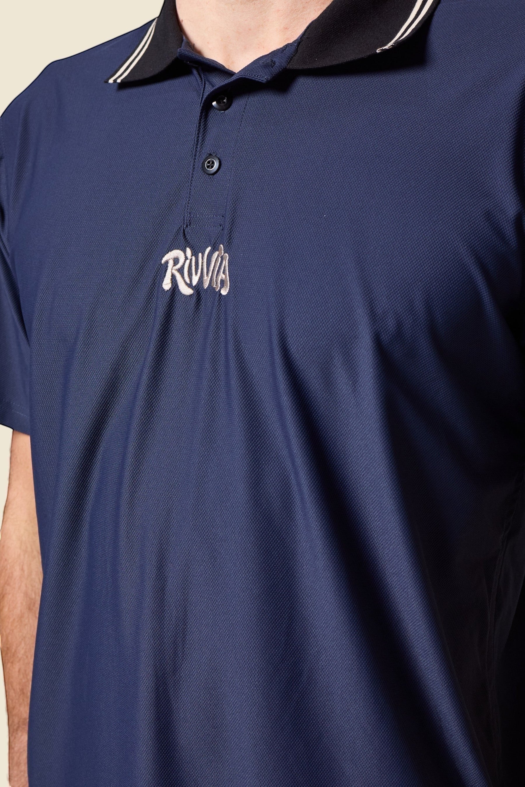 Keel Surf & Supply navy blue polo shirt with black collar featuring white and gold stripes, and embroidered chest logo.