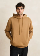 Man wearing a brown hoodie against a beige background