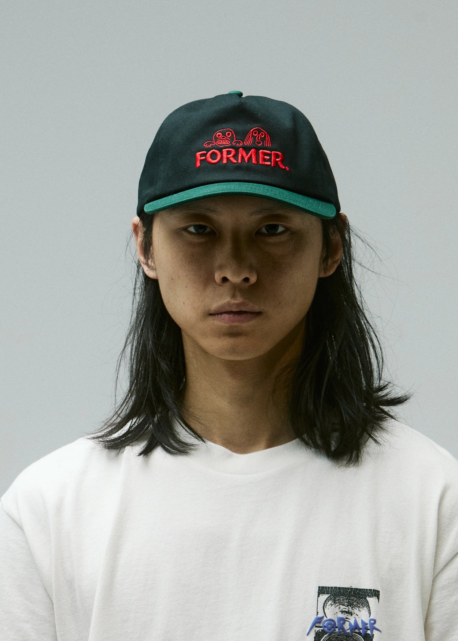 Person wearing a black cap with red text and a white t-shirt against a gray background