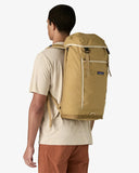 Man wearing a tan backpack with a visible brand logo on a white background