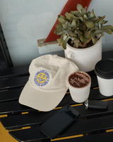 White cap with logo, black phone cases, and a plant on a table