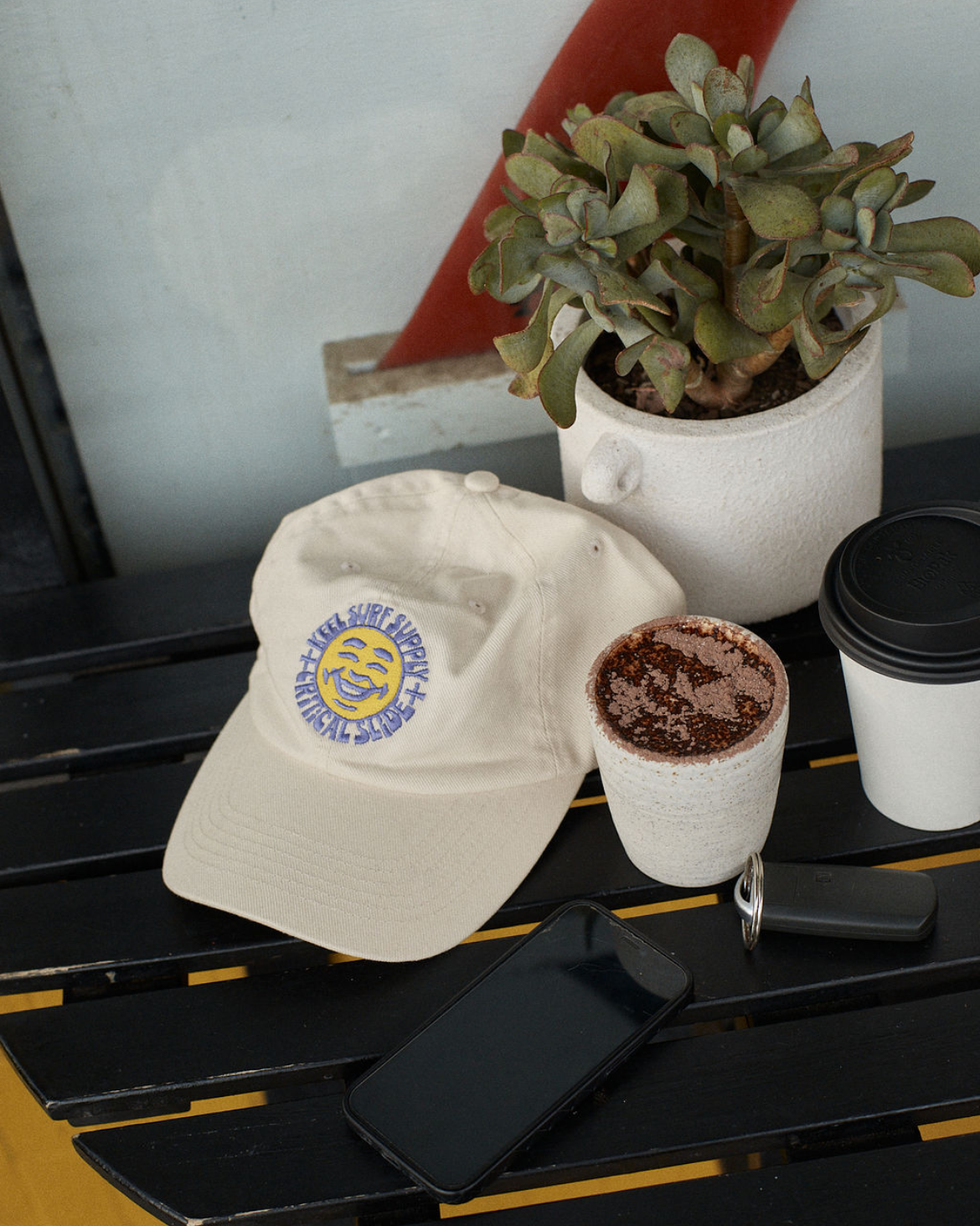 White cap with logo, black phone cases, and a plant on a table