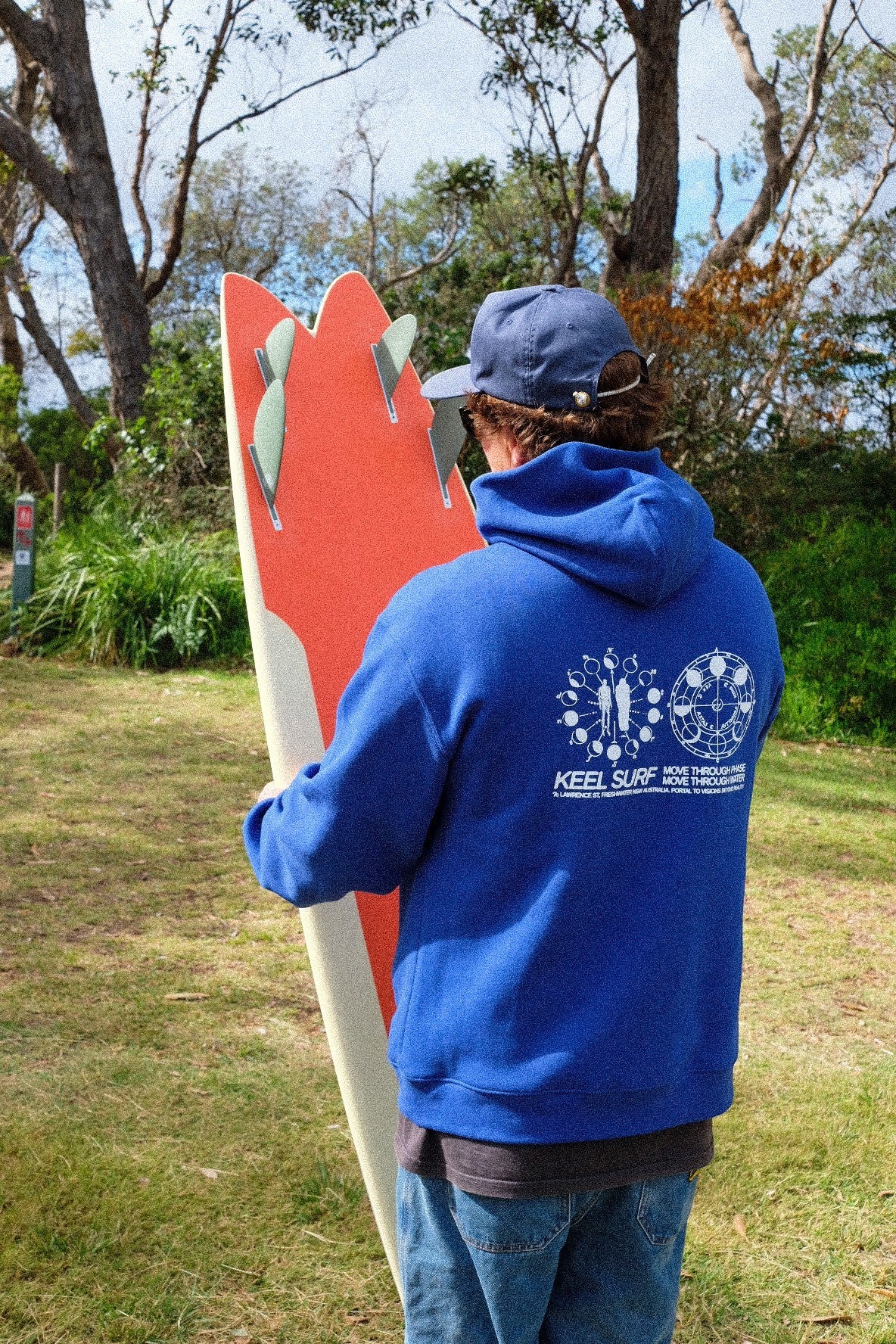 Keel Surf & Supply blue cotton blend hooded sweatshirt with graphic print on back, worn by a person holding a surfboard.