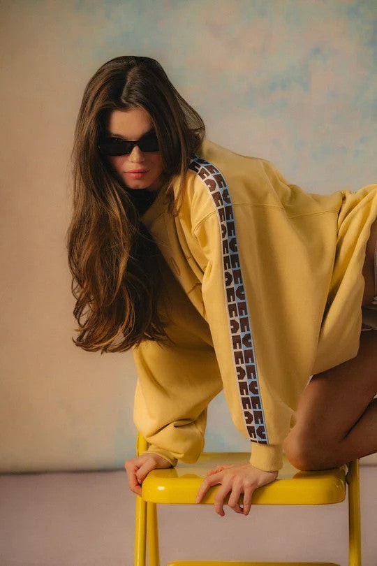 Keel Surf & Supply yellow cotton Delfino sweater with blue and brown logo tape on sleeves. Model wears sunglasses.